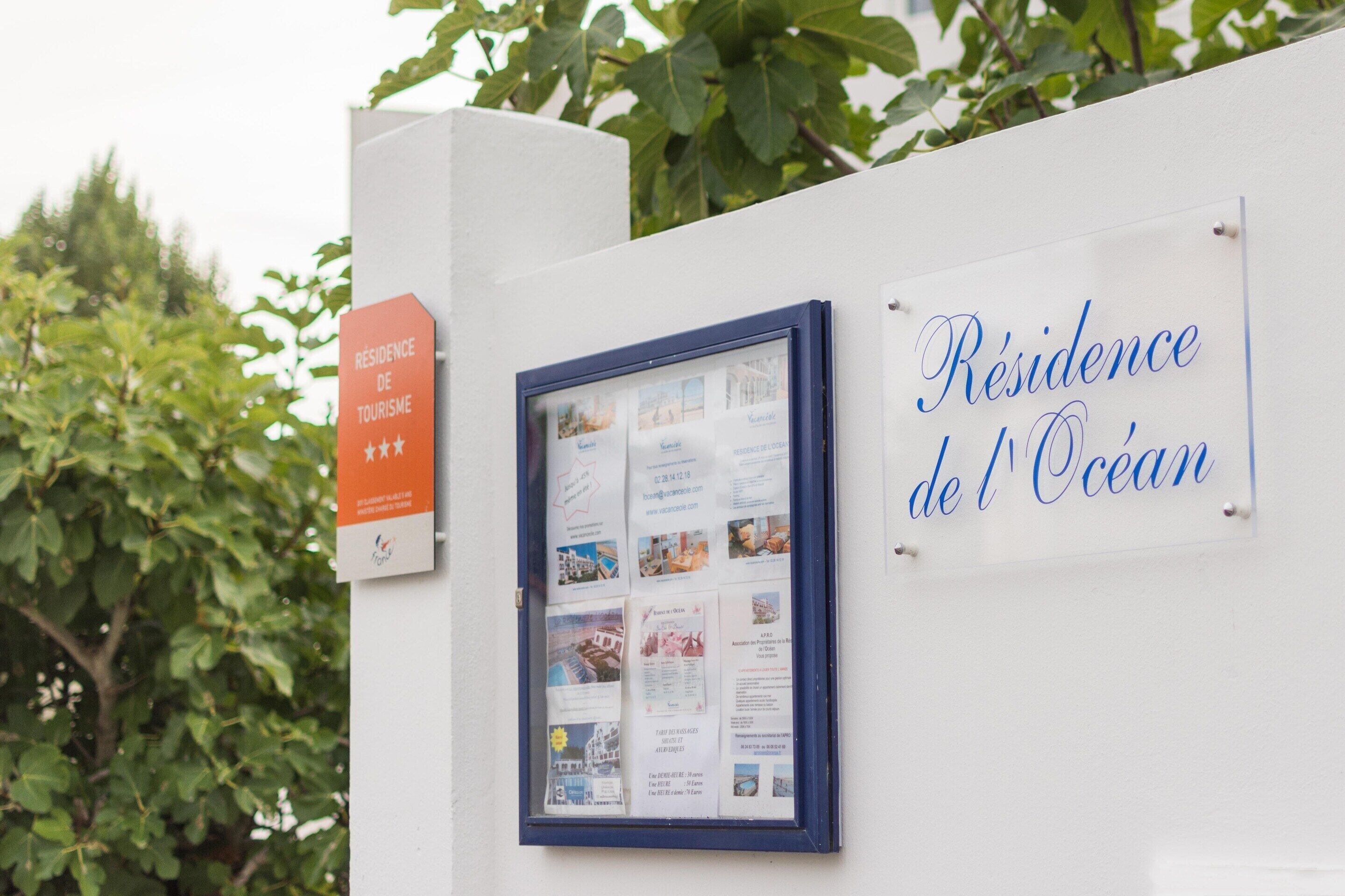 A sign with 'Résidence de l'Ocean' written in cursive, a framed informational display, and a red sign indicating 'Résidence de Tourisme.'