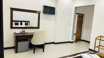 A hotel room with a bed, a desk with a chair, a small refrigerator, a television mounted on the wall, and a wooden door.