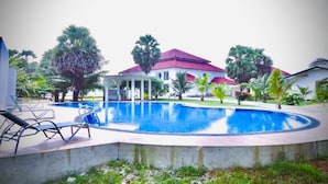 A swimming pool with lounge chairs, a covered seating area, and a building with a red roof.