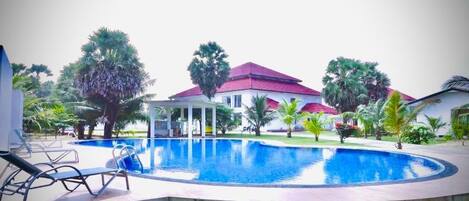 A swimming pool with lounge chairs, a covered seating area, and a building with a red roof.
