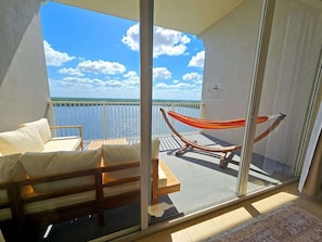 A balcony with a view of the sea, a hammock, and a seating area with cushions. - Lakefront Condo 1 Mile to Disney w/ Pool, Hot Tub (Orlando)