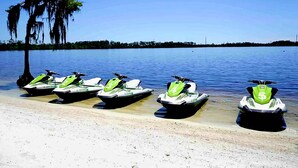 A row of jet skis on a sandy beach with a clear blue sky and a tree with hanging moss. - Lakefront Condo 1 Mile to Disney w/ Pool, Hot Tub (Orlando)