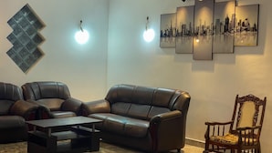 Un salón con un sofá modular, una mesa de centro, una alfombra estampada, una silla de madera y obras de arte colgadas en la pared.