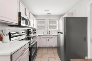 A modern kitchen with white cabinets, stainless steel appliances, and a black refrigerator. - FAMILY FUN BEACH HOUSE (Wildwood)