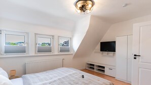 A bedroom with a bed, a TV mounted on the wall, and three windows with views. - Central vacation apartment in Arnsberg's old town (Arnsberg)