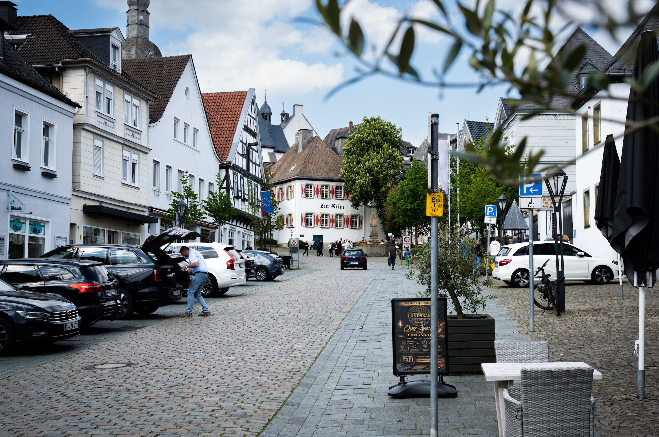 Une rue pavée bordée de bâtiments historiques, de voitures garées et d’un panneau indicateur.