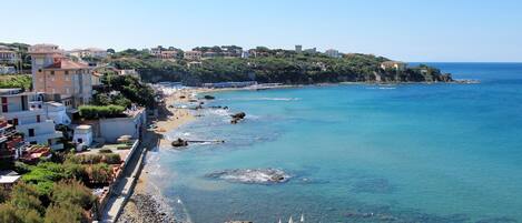 A coastal town with a beach, clear blue sea, and buildings along the shore.