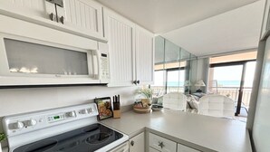 A modern kitchen with a stove, microwave, and white cabinets. - Oceanfront Condo with Heated Pool, 2 Balconies, Beach Access & Courts (Ocean City)