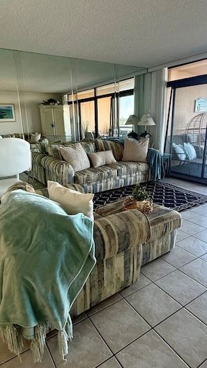 A living room with a sofa set, a large window, and a view of the outside.