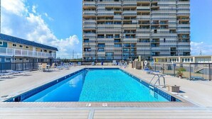 A hotel with a large swimming pool, multiple balconies, and a clear sky. - Oceanfront Condo with Heated Pool, 2 Balconies, Beach Access & Courts (Ocean City)