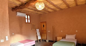A cozy hotel room with two beds, a wooden ceiling, a hanging light fixture, and a small table.