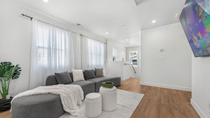 Uma sala de estar moderna com um sofá modular cinza, um tapete branco e um banquinho verde.