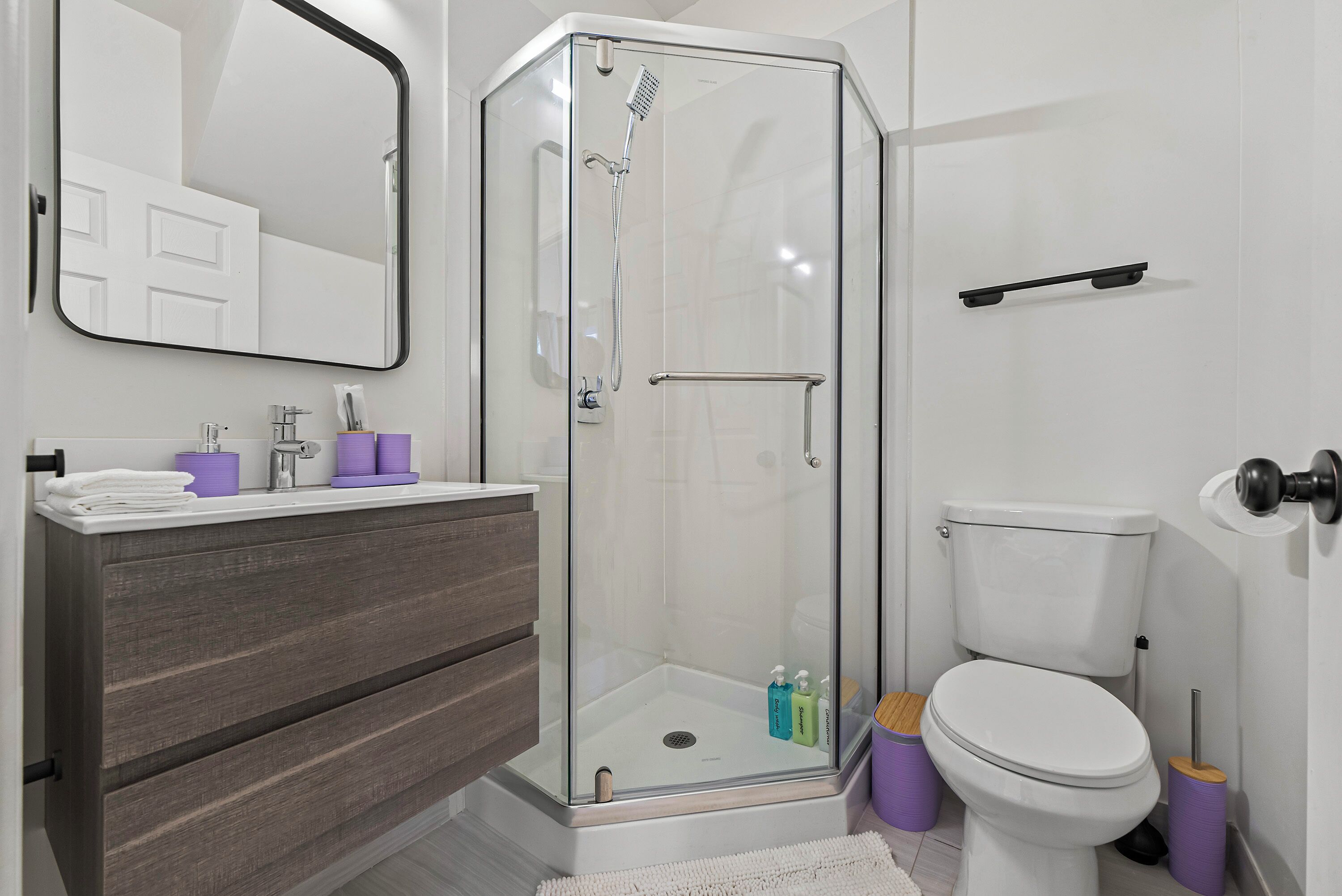 A modern bathroom with a glass-enclosed shower, a white toilet, and a vanity with a mirror.