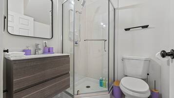 A modern bathroom with a glass-enclosed shower, a white toilet, and a vanity with a mirror.