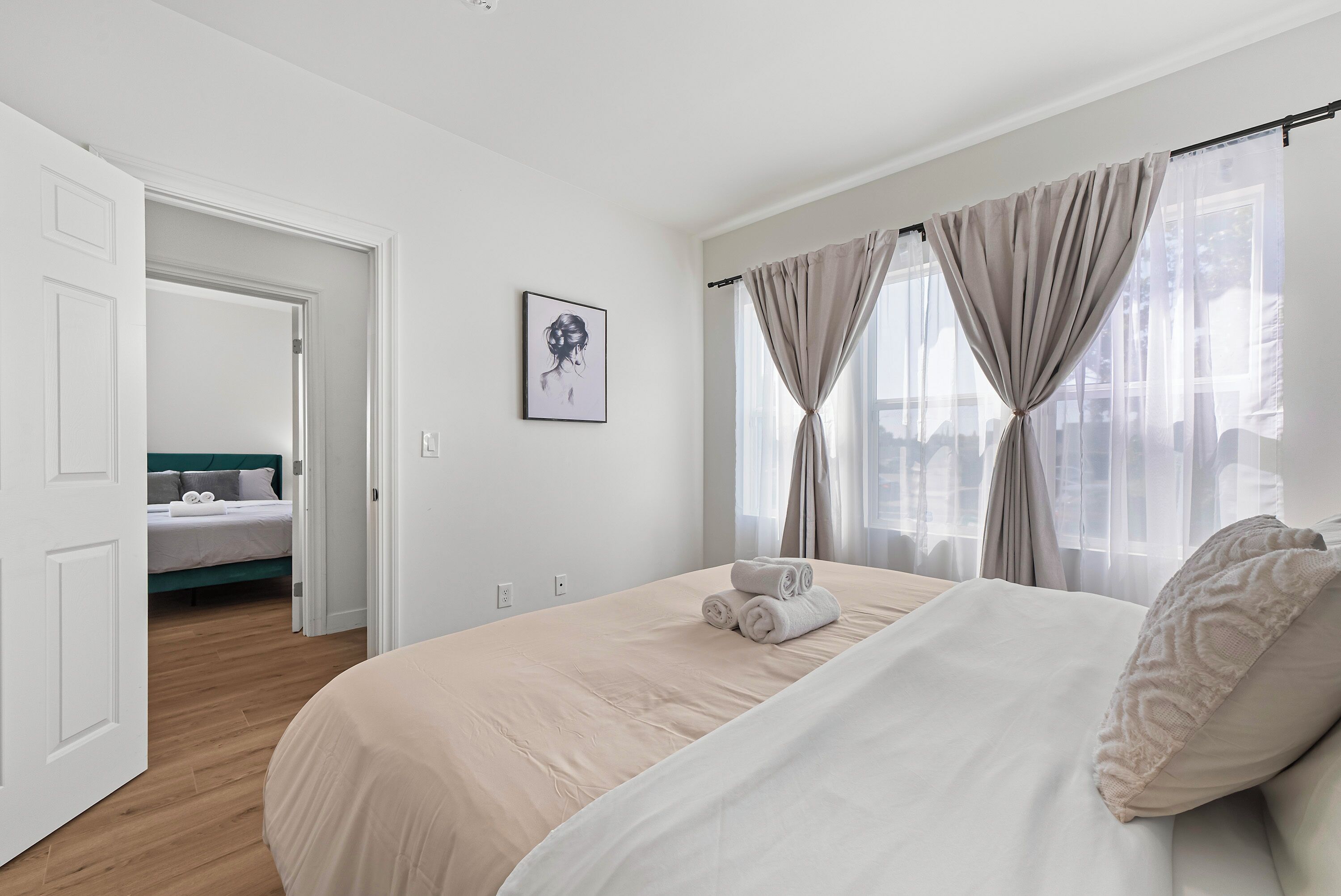 Une chambre d’hôtel avec un grand lit, une table de chevet, une fenêtre avec des rideaux et une porte donnant sur une autre pièce.