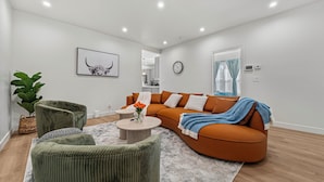 Uma sala de estar moderna com um sofá de canto, poltronas verdes, uma mesa de centro e uma planta grande.