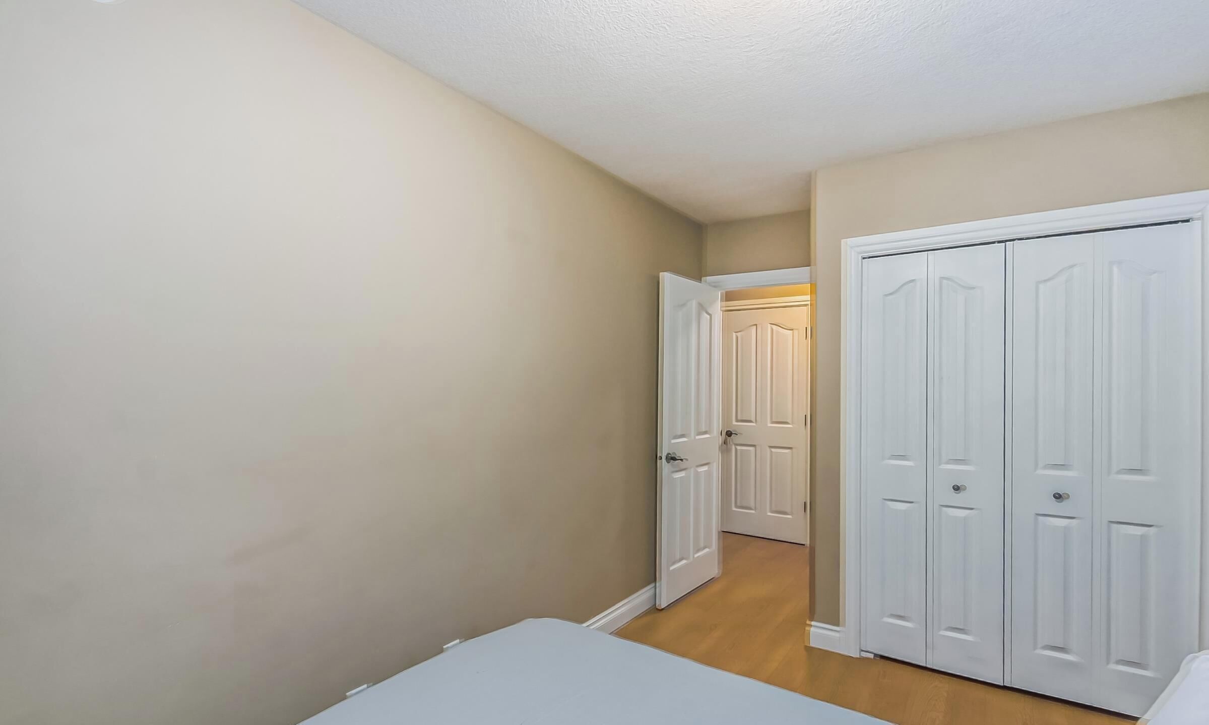 Un couloir aux murs de couleur beige et au plancher en bois, qui mène à un ensemble de portes doubles blanches.