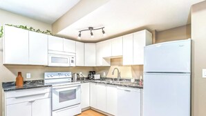 Una cocina moderna con armarios blancos, horno empotrado, microondas, lavabo y refrigerador.