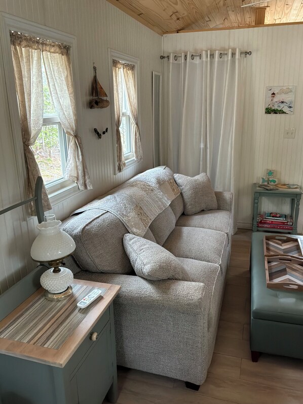 A cozy room with a sofa, a lamp, a small table, and a side table with books and decorative items.