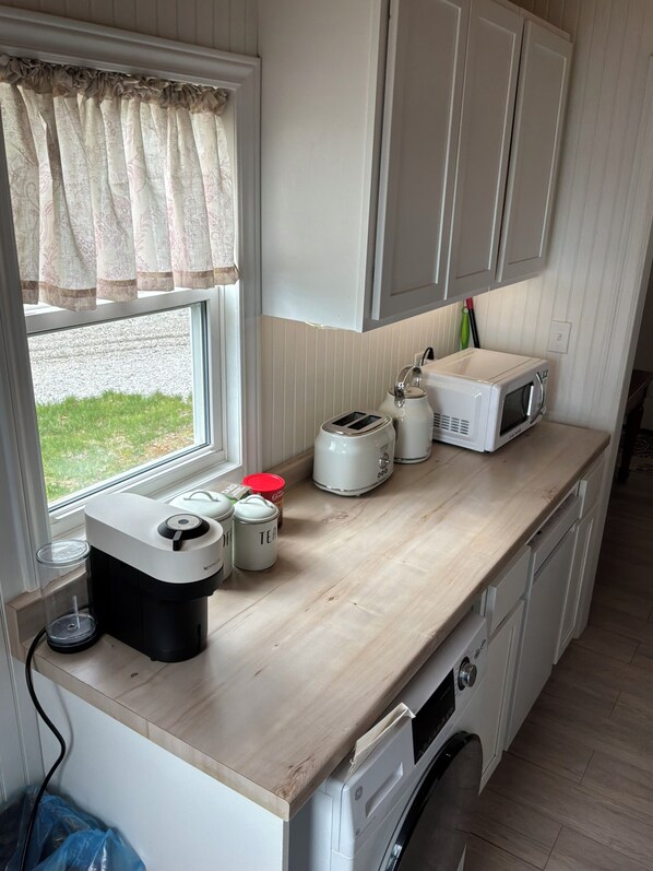 Eine kompakte Küche mit Waschmaschine, Mikrowelle, Toaster und Kaffeemaschine auf der Arbeitsplatte.