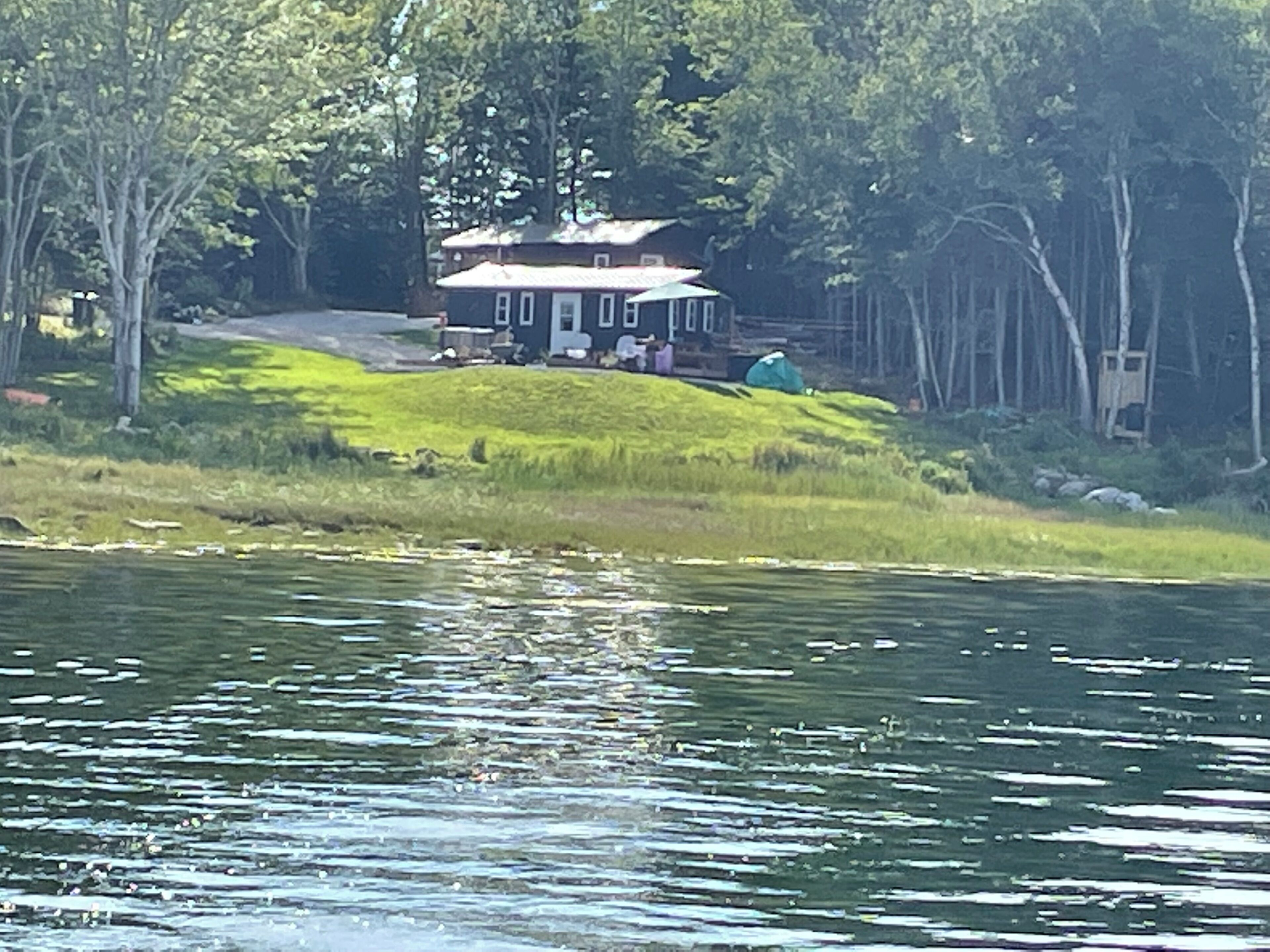 A house with a front porch, surrounded by trees and a body of water.