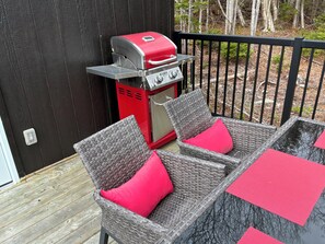 A patio with wicker chairs and red cushions, a red grill, and a black fence.