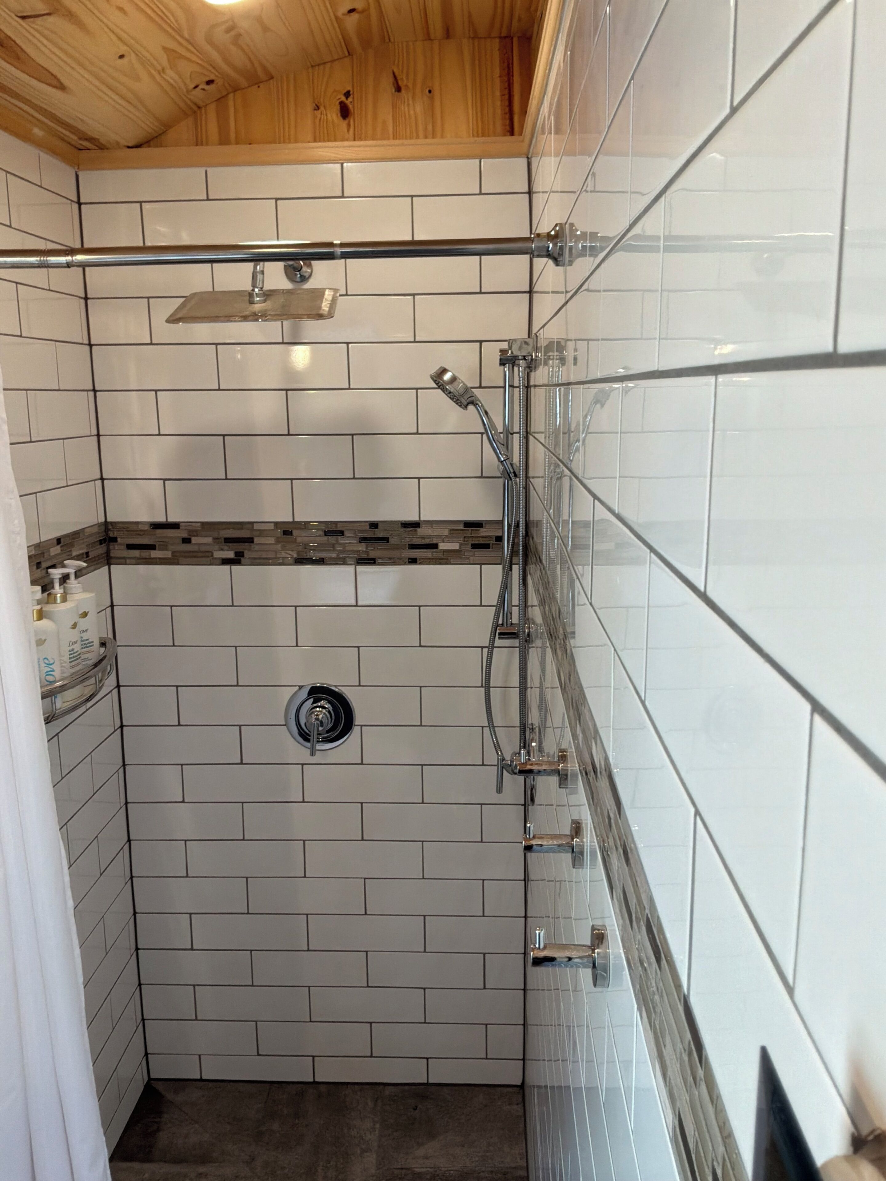A shower with a glass door, a wooden ceiling, and a tiled wall with a patterned border.