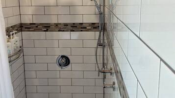 A shower with a glass door, a wooden ceiling, and a tiled wall with a patterned border.