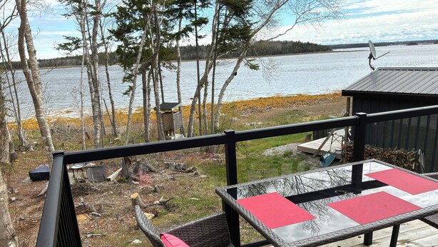 Una terraza con sillas de mimbre y una mesa, con vista a un lago con árboles y un muelle.