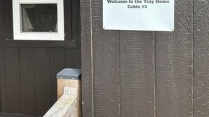 Entrada de una cabaña de madera con un letrero de bienvenida, una ventana con cortinas y un farol.