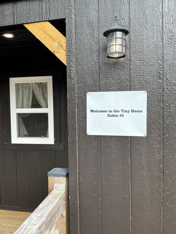 A wooden cabin entrance with a welcome sign, a window with curtains, and a lantern.