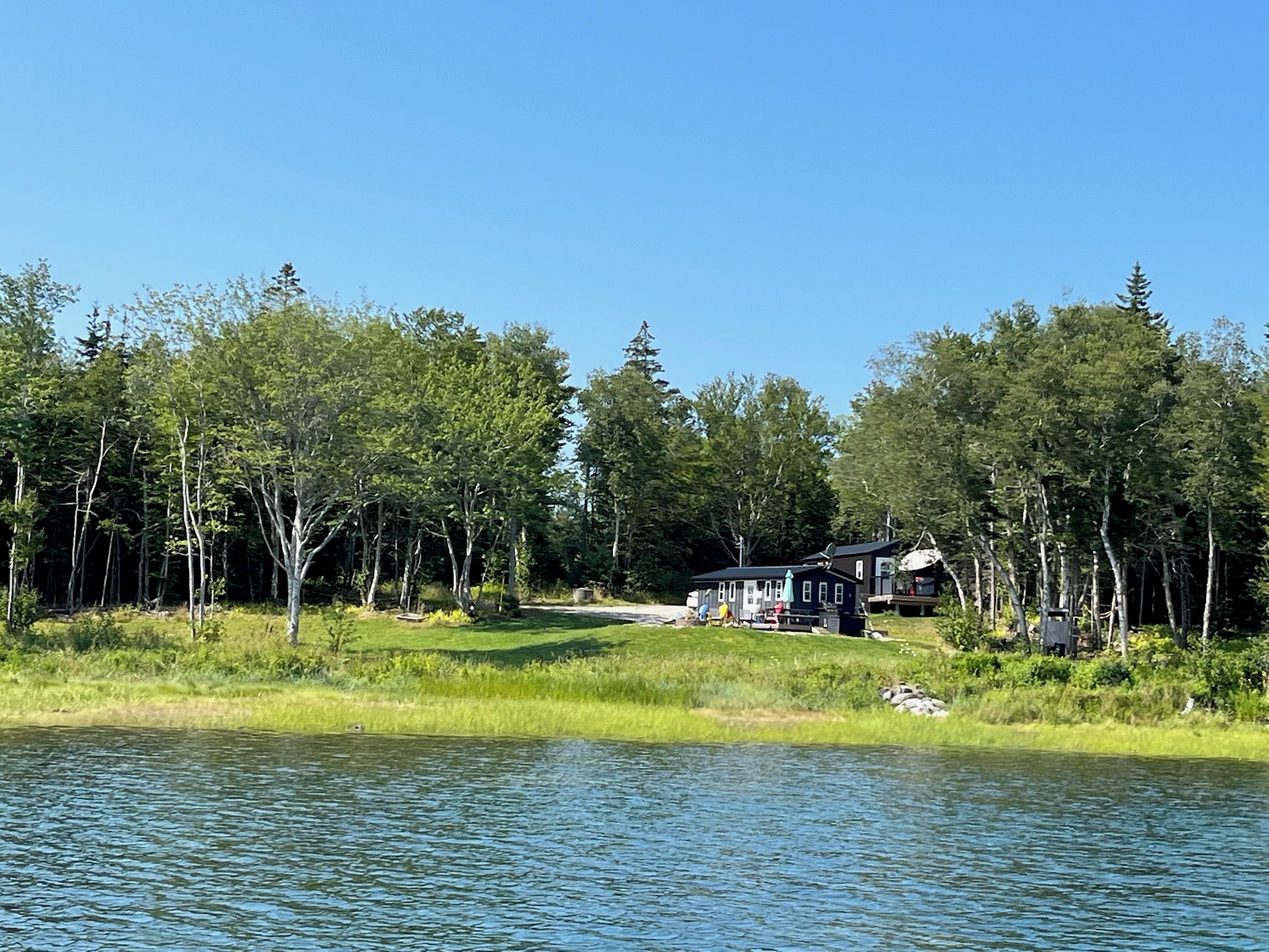 A lakeside cabin with a deck and a boat dock, surrounded by dense forest.