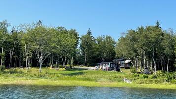 A lakeside cabin with a deck and a boat dock, surrounded by dense forest.
