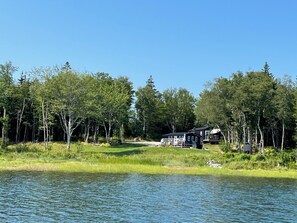 A lakeside cabin with a deck and a boat dock, surrounded by dense forest.