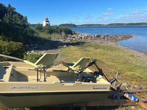 A boat named 'SPORTSMAN8' with two chairs and a fishing rod, docked near a rocky shore with a lighthouse in the background.