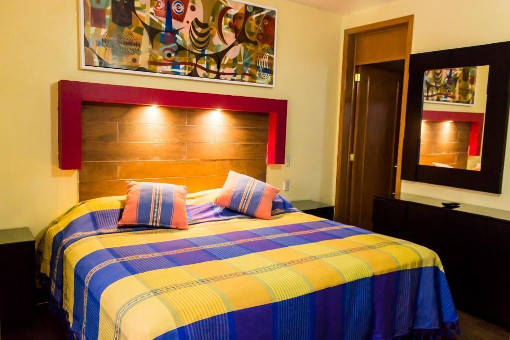 Una habitación de hotel con una cama, cabecera, un cuadro y un espejo.