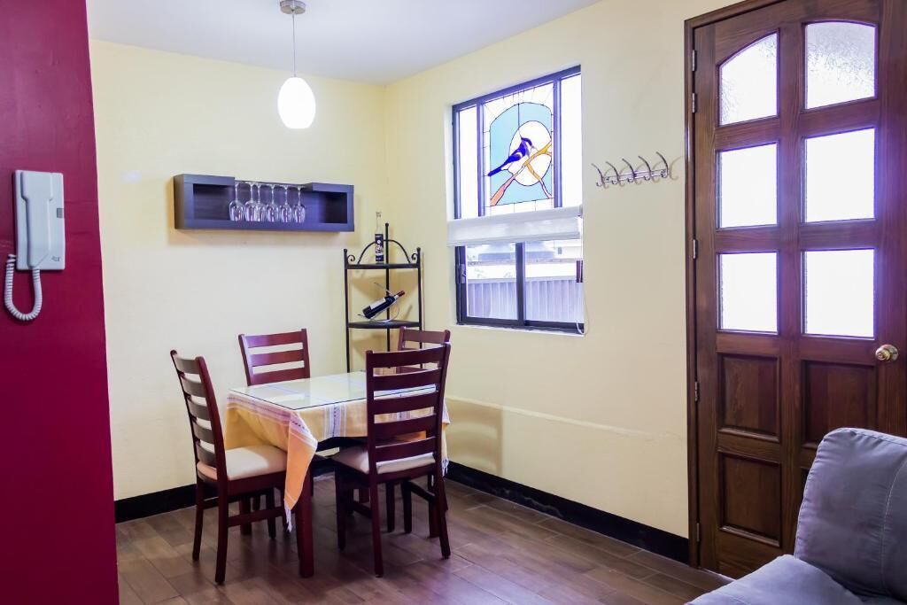 Un comedor con una mesa y sillas, un ventanal de vitral, una puerta y un teléfono fijo en la pared.