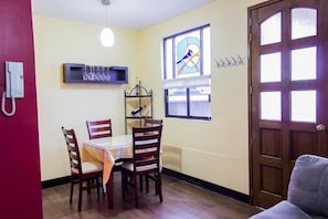 Un comedor con una mesa y sillas, un ventanal de vitral, una puerta y un teléfono fijo en la pared.
