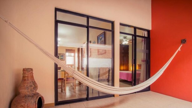 A room with a hammock, a large vase, and a sliding glass door leading to another room. - Casa del Barrio (Oaxaca)