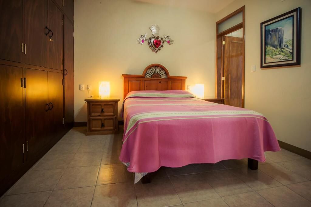 A bedroom with a bed, wooden wardrobe, bedside lamps, and a wall-mounted decorative piece.