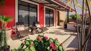 A red building with large windows, outdoor seating, and potted plants. - Casa del Barrio (Oaxaca)
