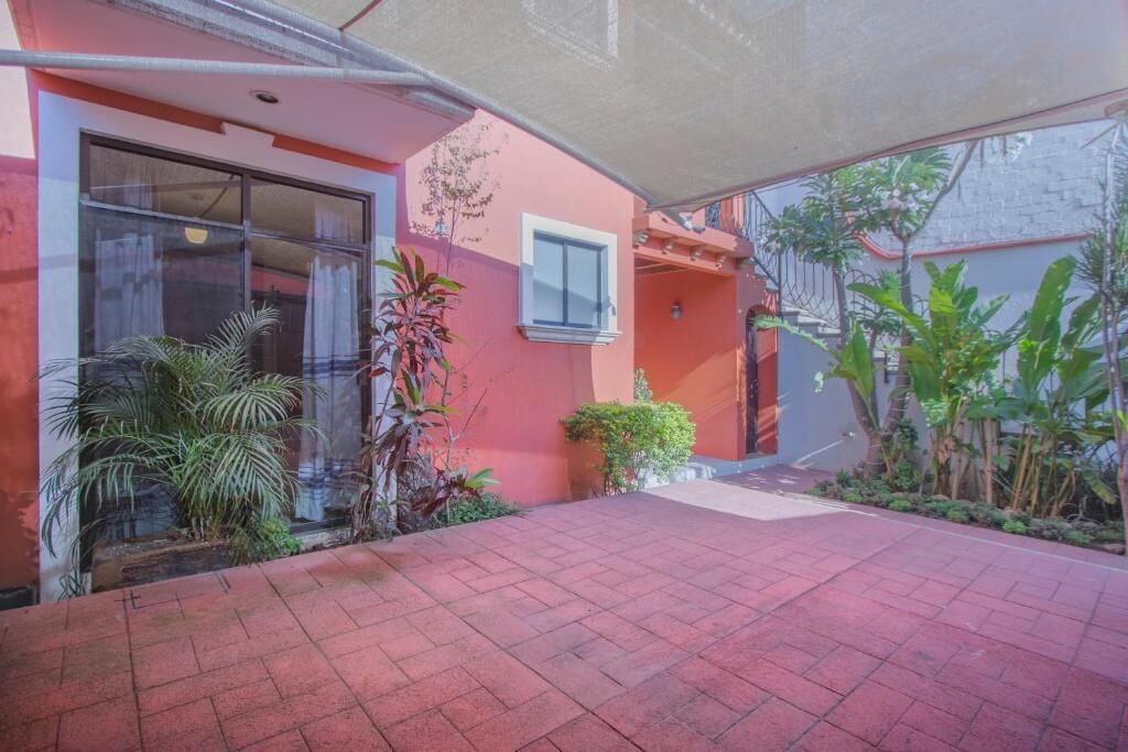 A building with a red exterior, a covered patio area, and various plants.