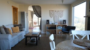 Ein Wohnzimmer mit Sofa, Couchtisch, Bücherregal und Blick durch ein großes Fenster.