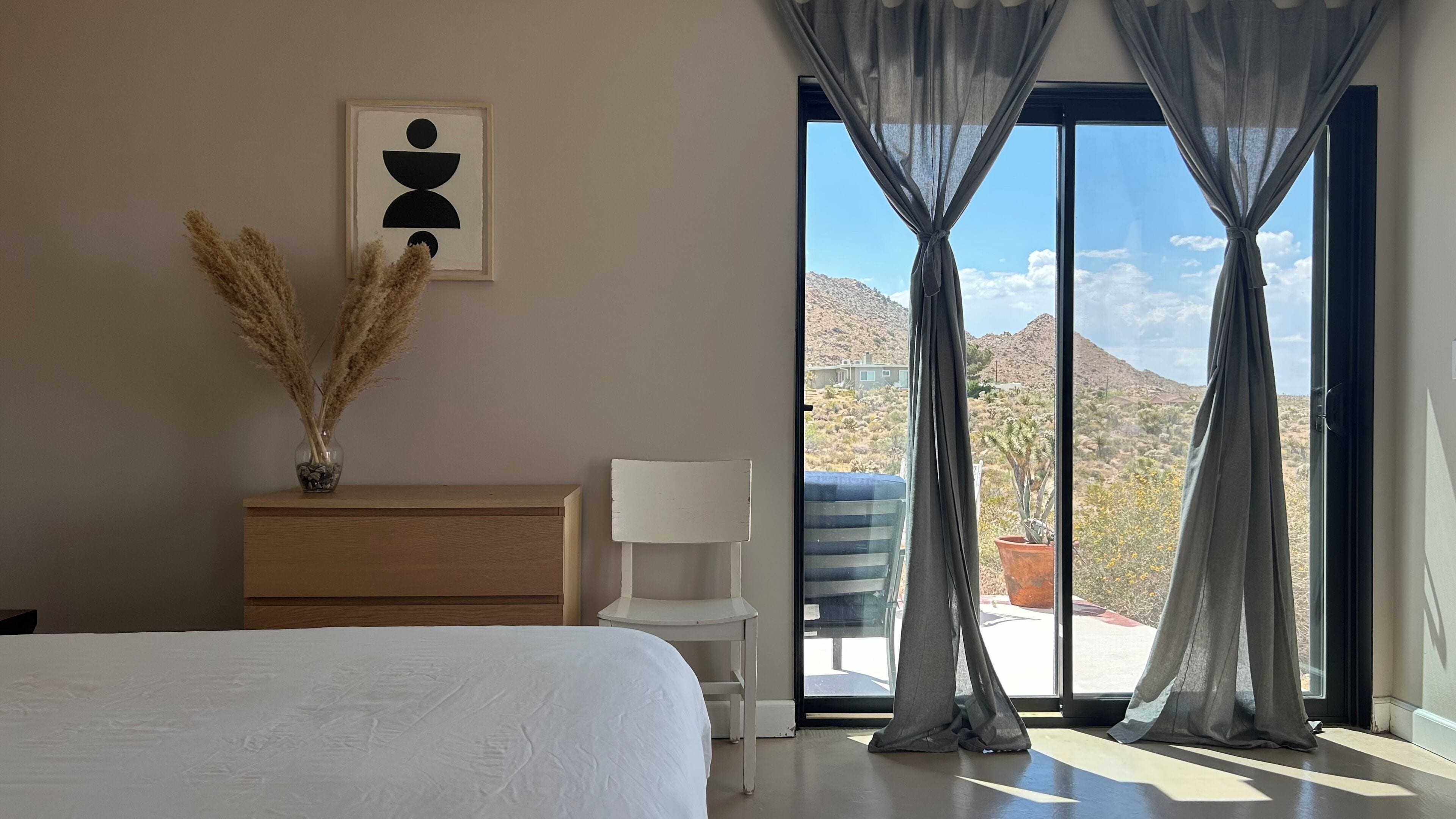 Une chambre à coucher comprenant un lit, une commode, une chaise, une fenêtre avec des rideaux et une vue sur un paysage désertique.