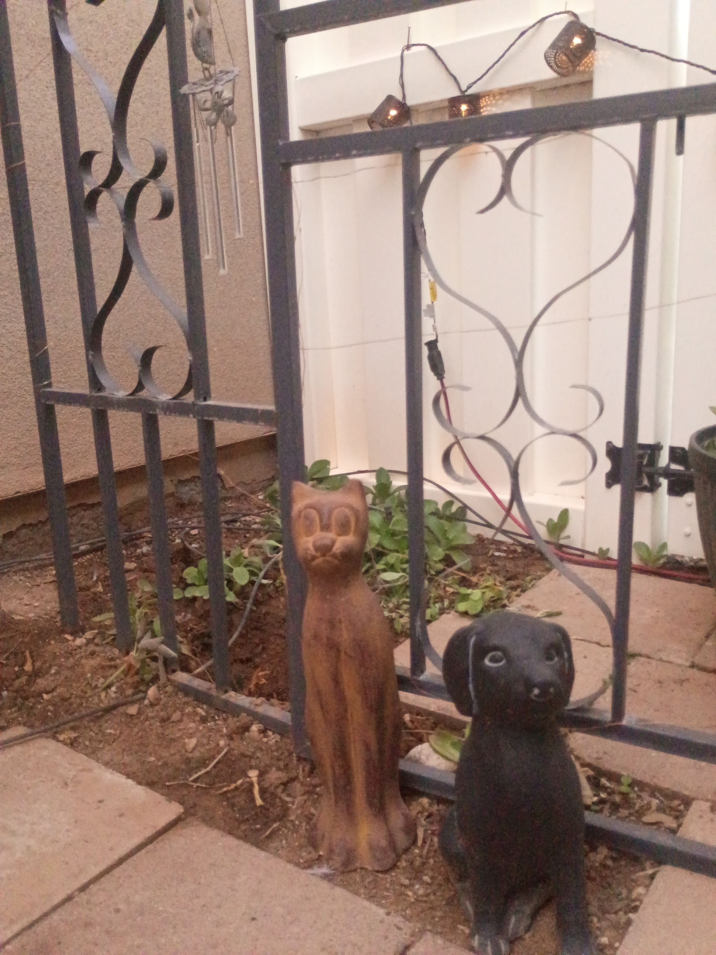 Ein schmiedeeisernes Tor mit Zierornamenten, eine Holzkatze und eine schwarze Hundefigur.