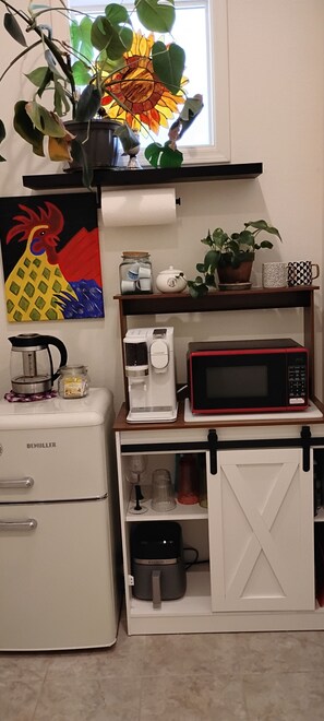 Een keuken met een koffiezetapparaat, een magnetron, een koelkast, een potplant en een schilderij.