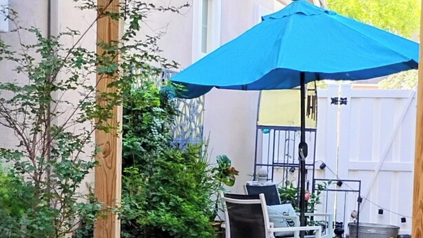 A patio area with a stone floor, a blue umbrella, a white chair, and a table.