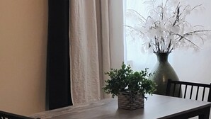 A dining area with a table, chairs, a vase with flowers, and a window with curtains.