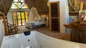 Una habitación con una bañera grande, una cama con dosel, una mecedora de madera y vistas a palmeras a través de las ventanas.