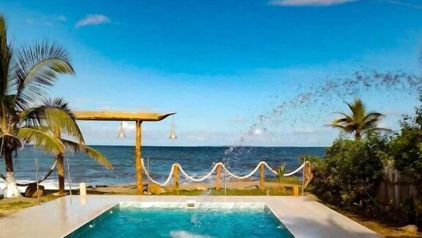 Una piscina con vista al océano, rodeada de palmeras y una pérgola de madera.